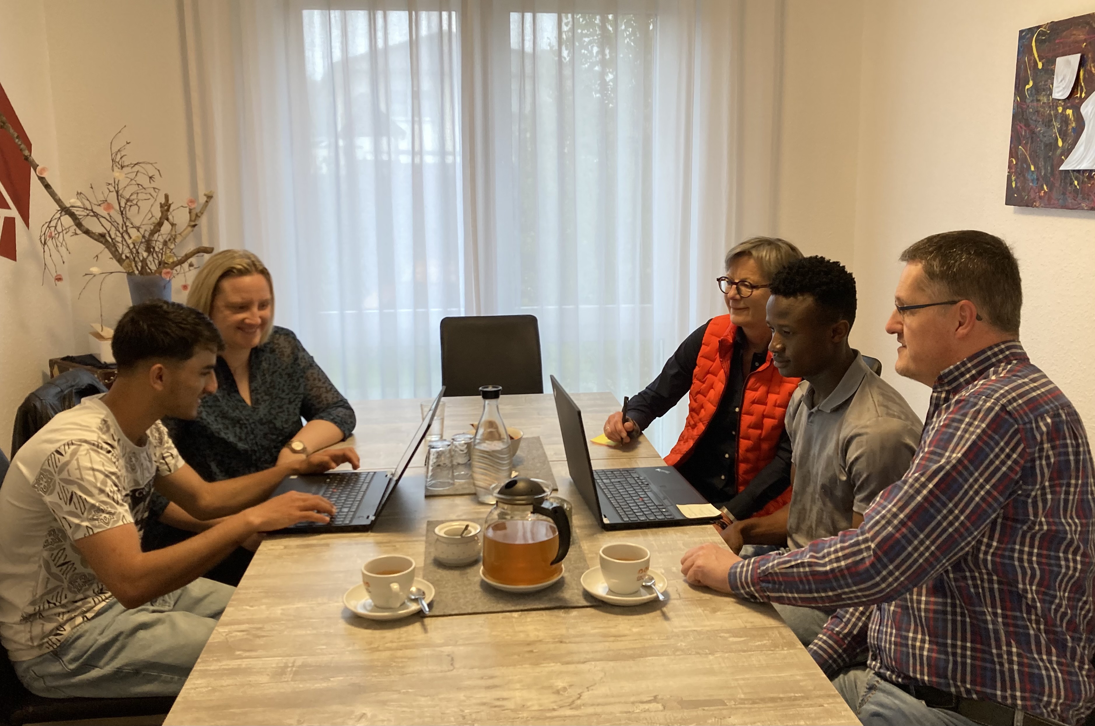 Aslam und seine Vormundin Tanja Schreiber (links) arbeiten mit Bernd Silkens, Mamoudou und seiner Vormundin Magga Dorissen-Schröders (rechts) an den Laptops; Foto: Kreis Heinsberg